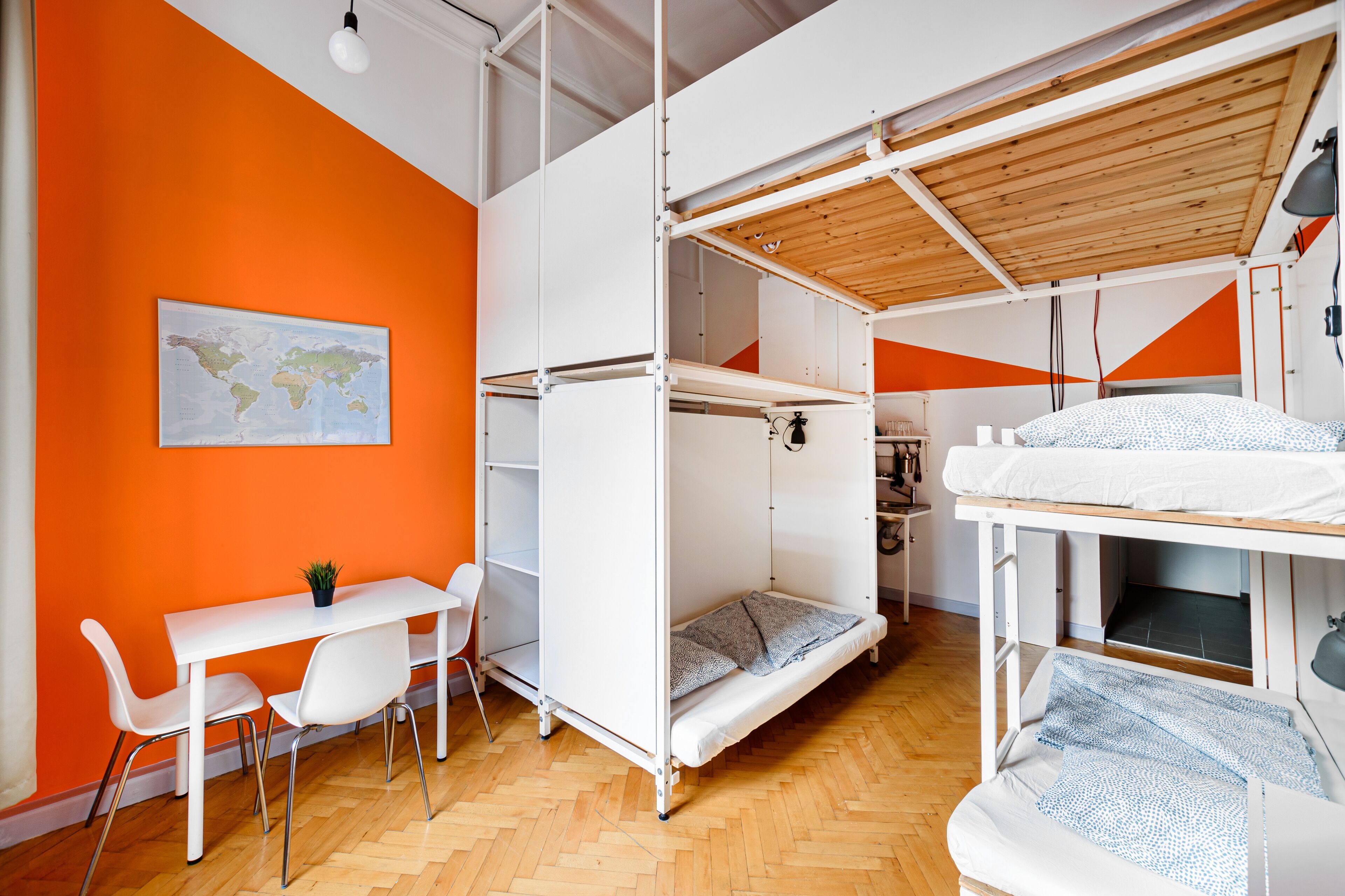Habitación pequeña con literas, un escritorio con sillas y un mapa mundial en la pared.