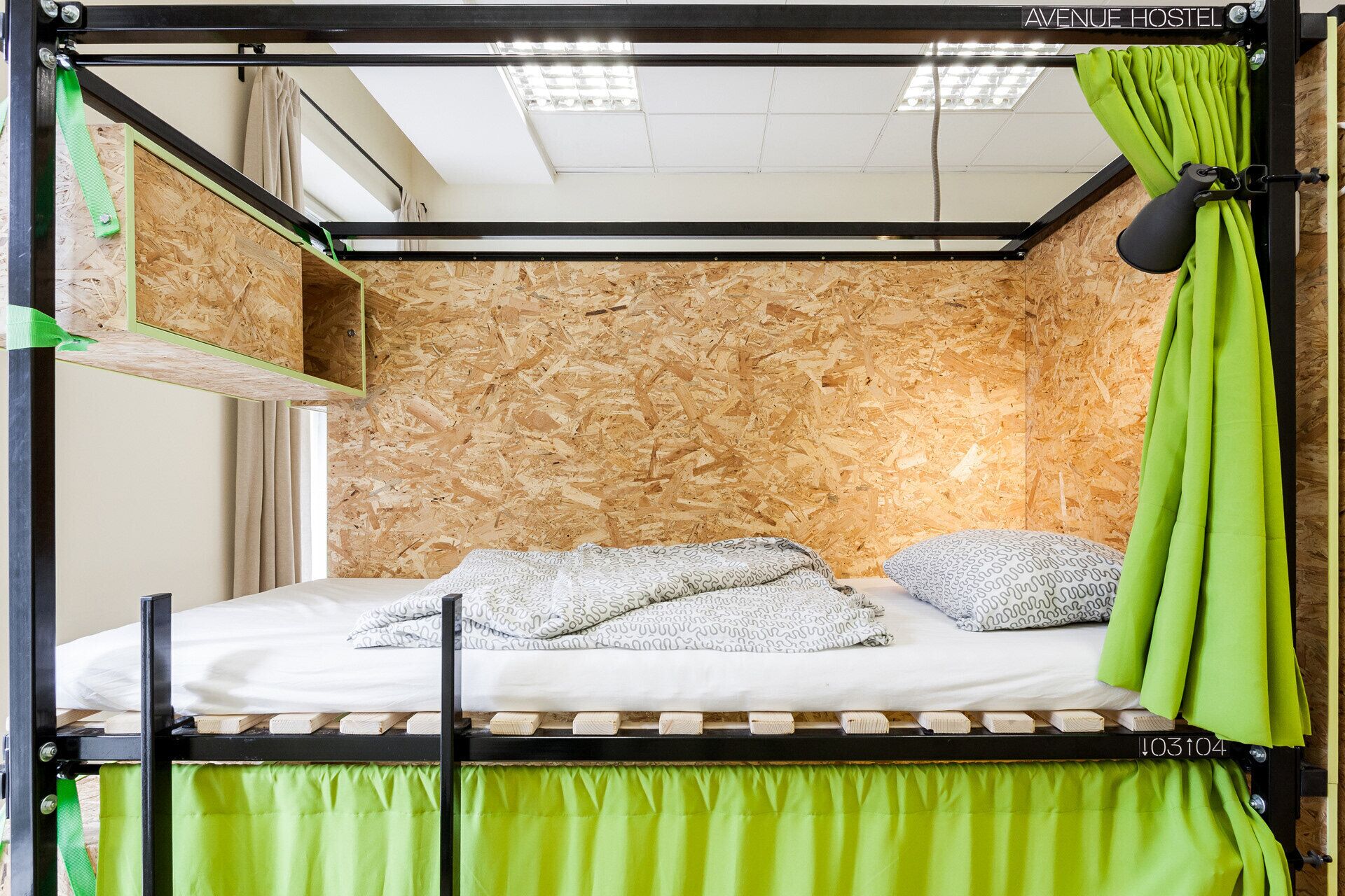 Una cama litera con cabecera de madera, una cortina verde y una lámpara colgante.