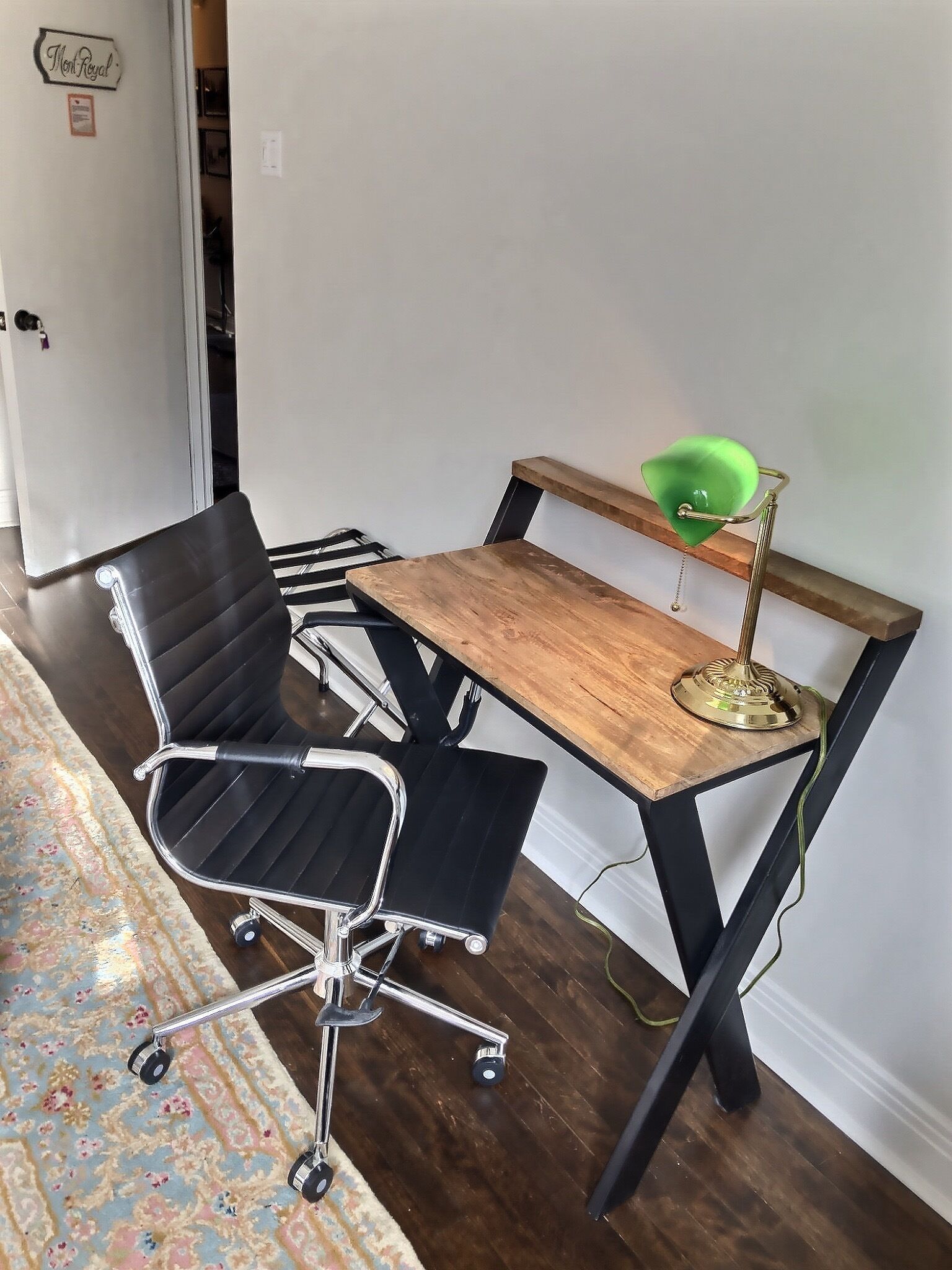 A small office space with a wooden desk, a black office chair, and a green desk lamp.