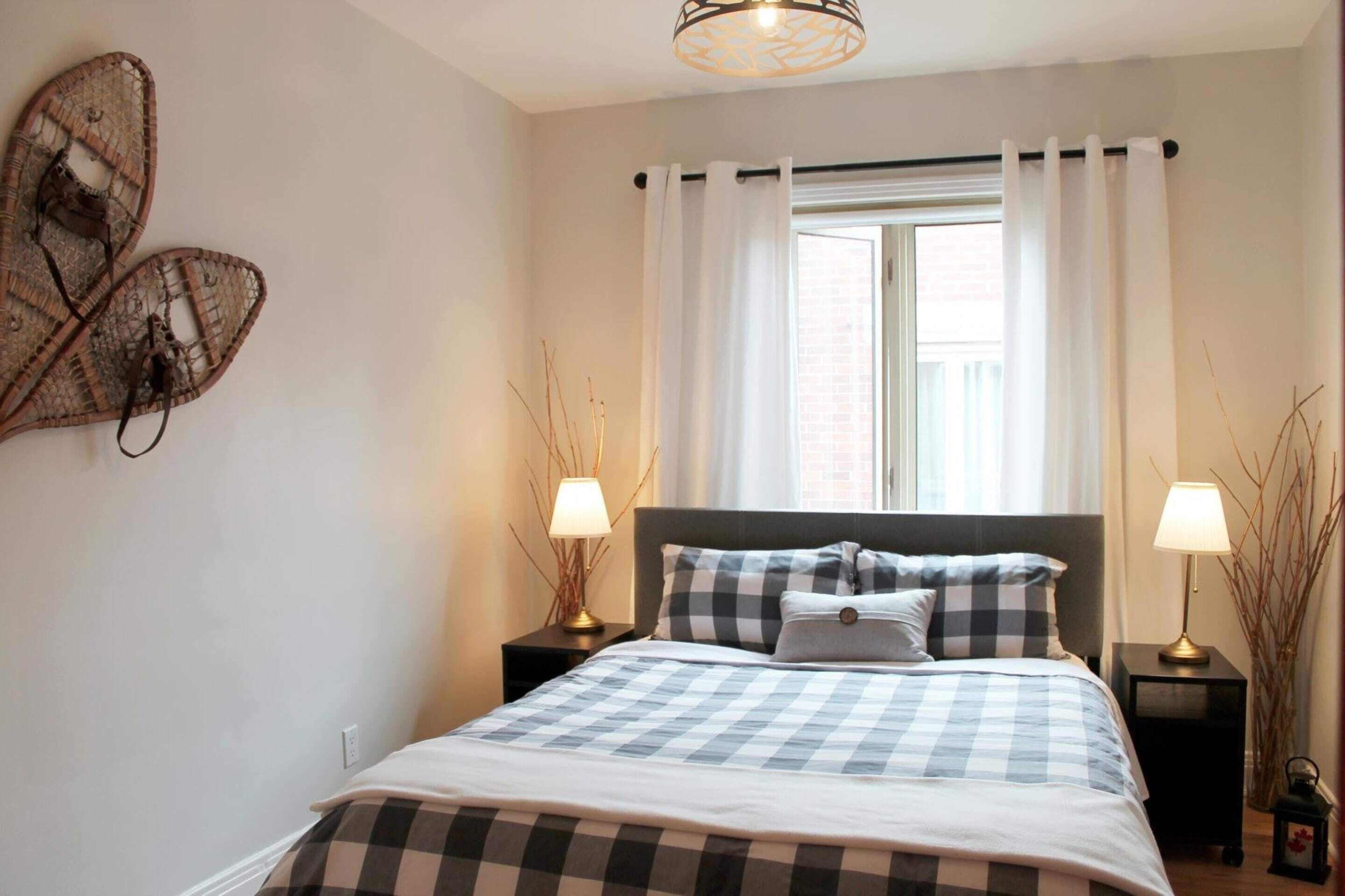 A neatly arranged bedroom with a bed, two bedside tables, a window with curtains, and wall art.