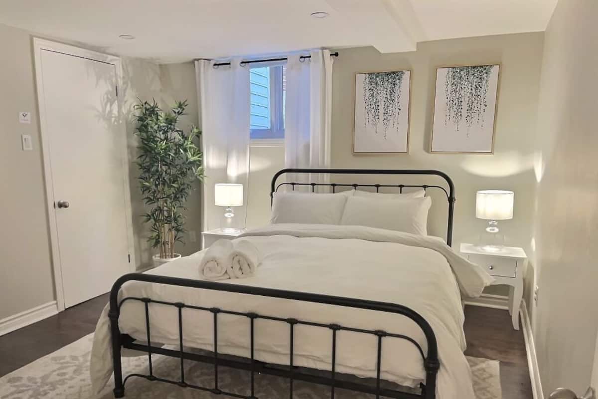Un dormitorio ordenado con cama, mesitas de noche, una planta en maceta y obras de arte en las paredes.