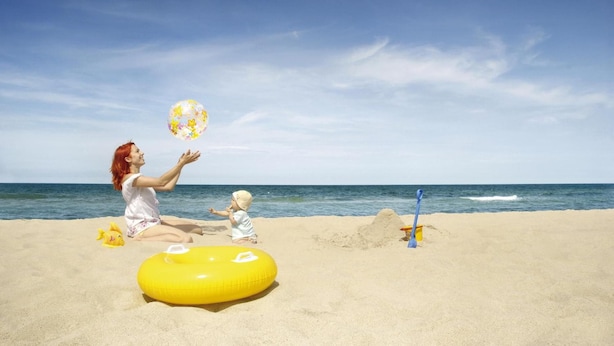 A beach scene with a woman and a child playing with a ball. - Hotel Sonneninsel Fehmarn (Fehmarn)