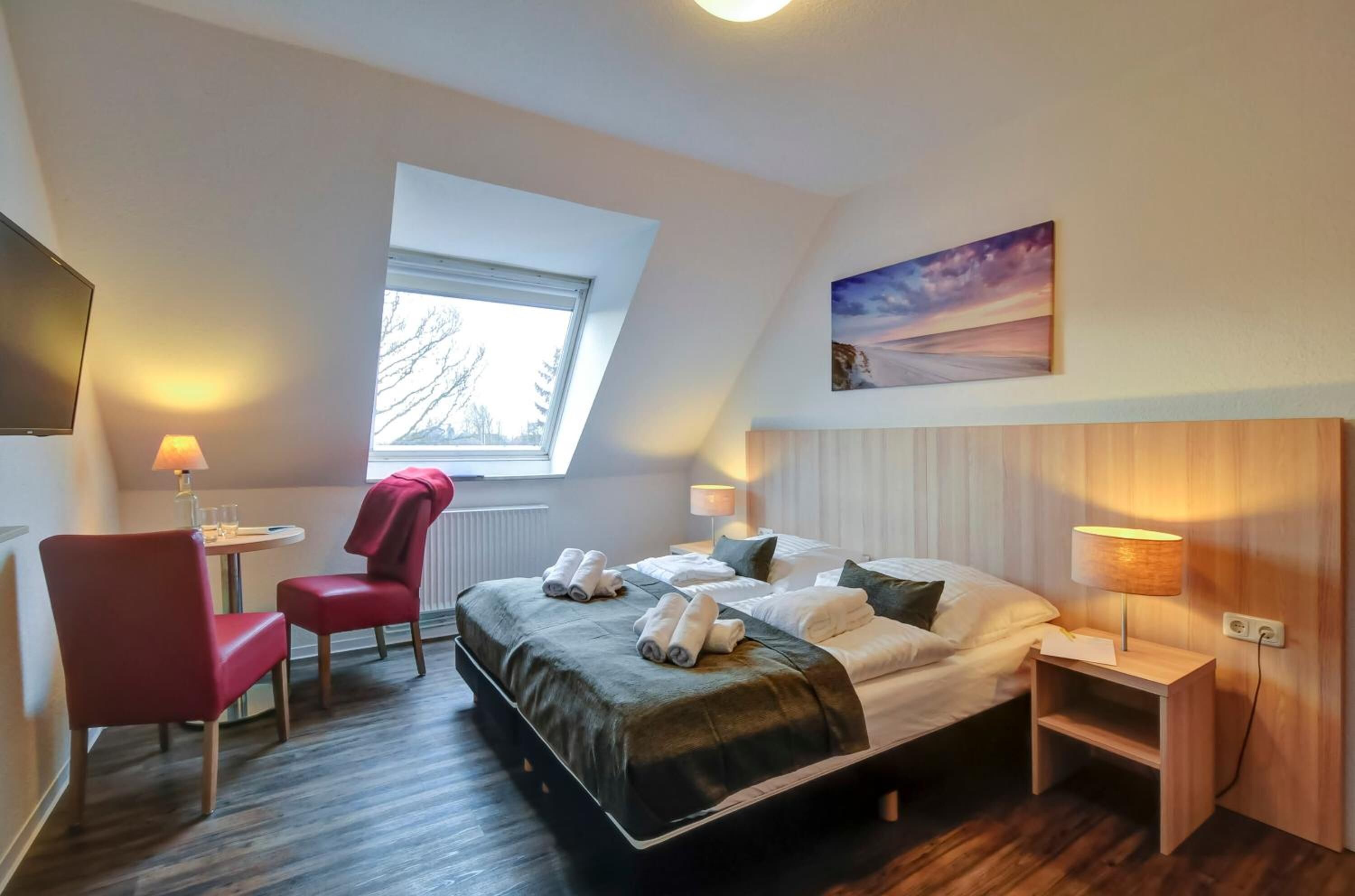 Habitación de hotel con cama, escritorio, silla, ventana y un cuadro en la pared.