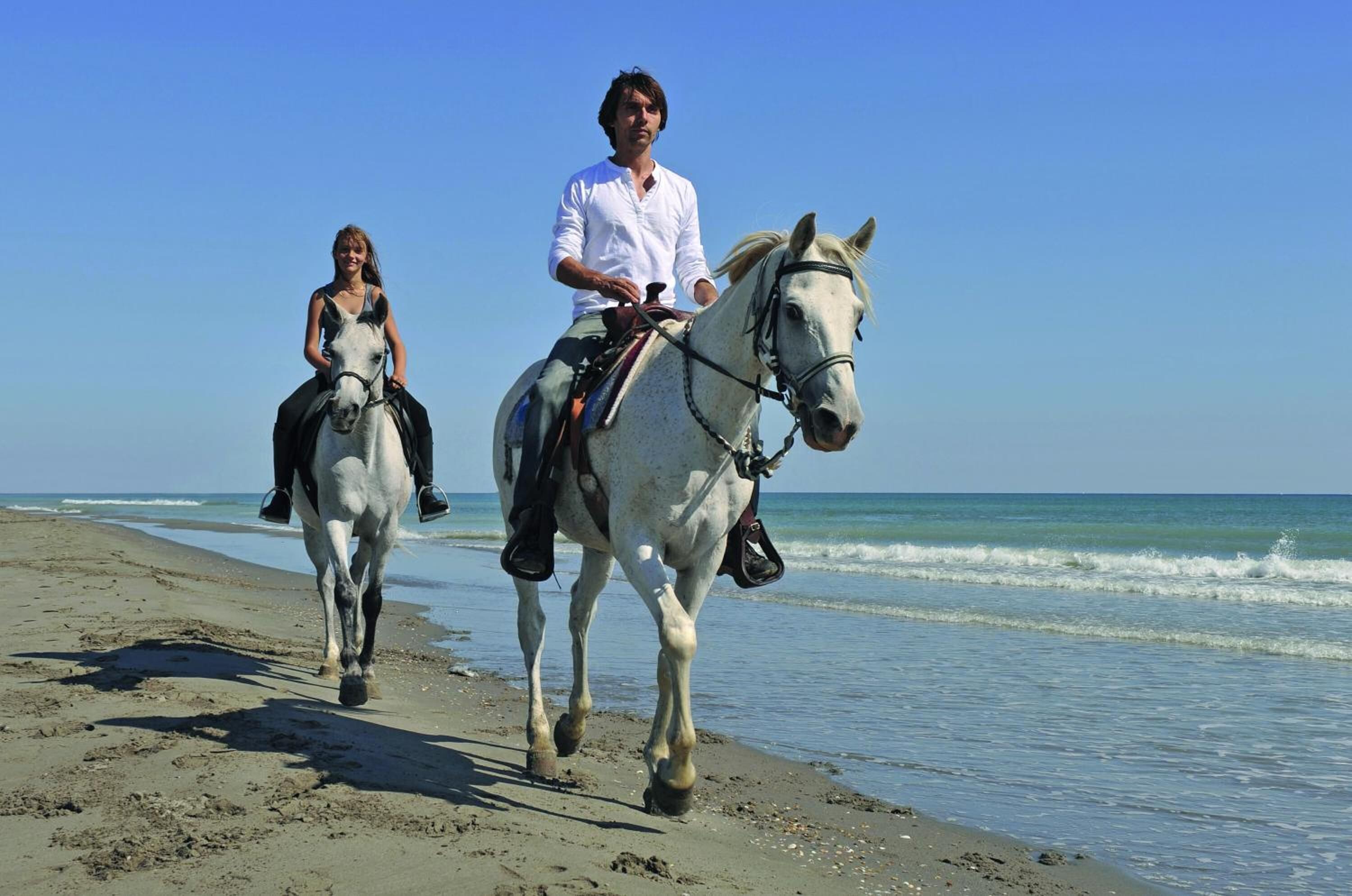 Two people riding horses on a beach.