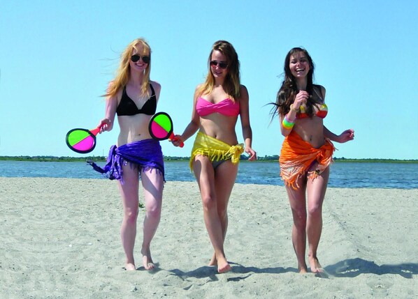 Tres personas caminando sobre una playa arenosa sosteniendo objetos coloridos.