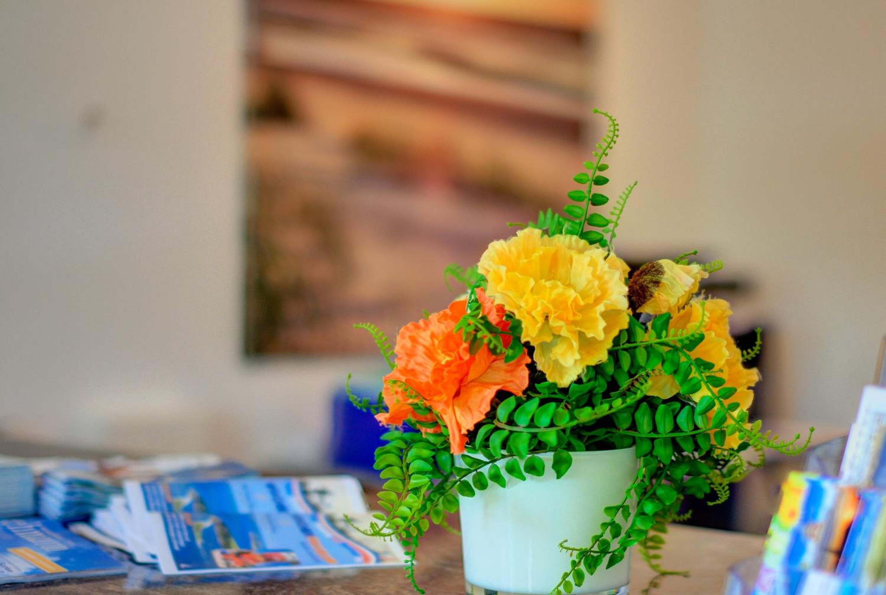 Un vase blanc contenant un bouquet de fleurs jaunes et oranges, ainsi que des feuilles vertes, est posé sur une table.