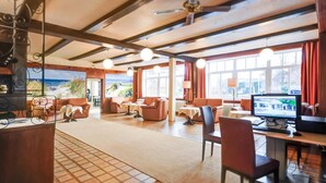 A spacious hotel lobby with a large TV, comfortable seating, and a view of the outdoors. - Hotel Sonneninsel Fehmarn (Fehmarn)