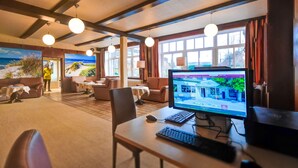 A room with a wooden ceiling, round pendant lights, a large window with curtains, a computer on a desk, and a view of the outdoors. - Hotel Sonneninsel Fehmarn (Fehmarn)