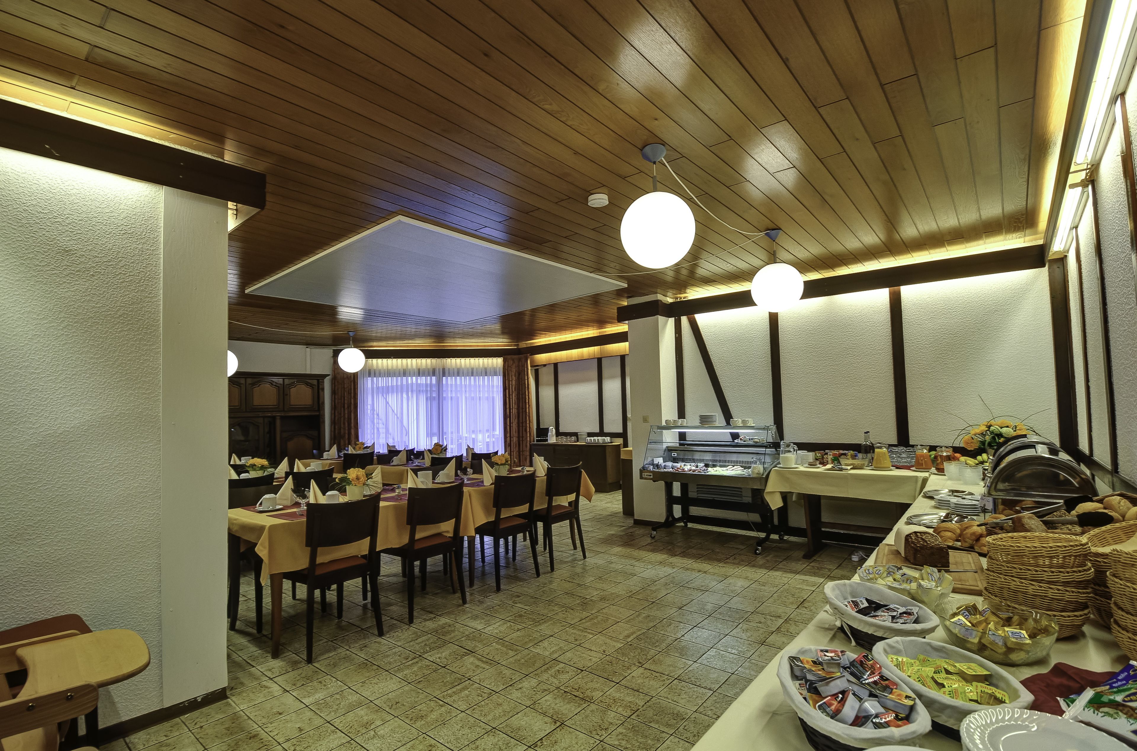 A dining area with wooden ceiling, tables with yellow tablecloths, and a buffet with various food items.