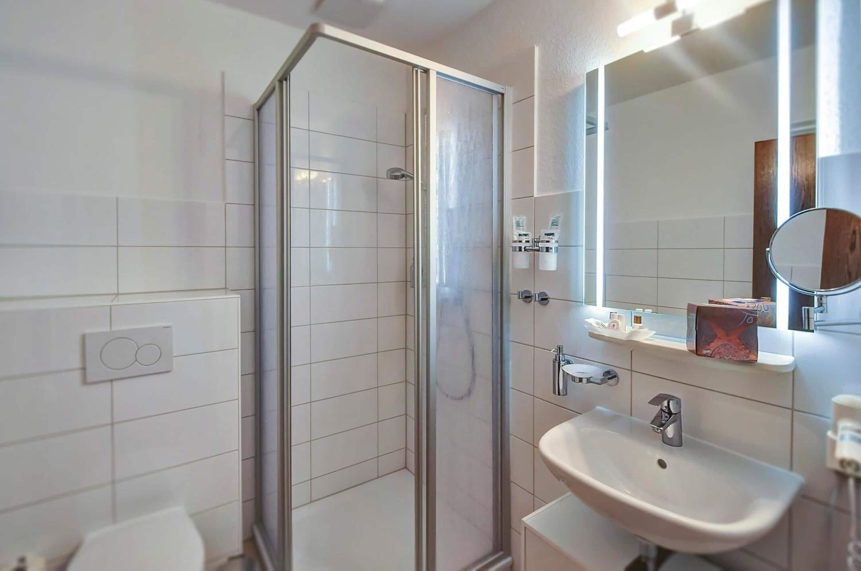 Een moderne badkamer met een douchecabine van glas, een witte wastafel en een spiegel met een ronde lijst.