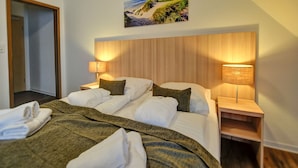 A hotel room with a large bed, two bedside tables with lamps, a painting of a beach scene, and a wooden headboard. - Hotel Sonneninsel Fehmarn (Fehmarn)