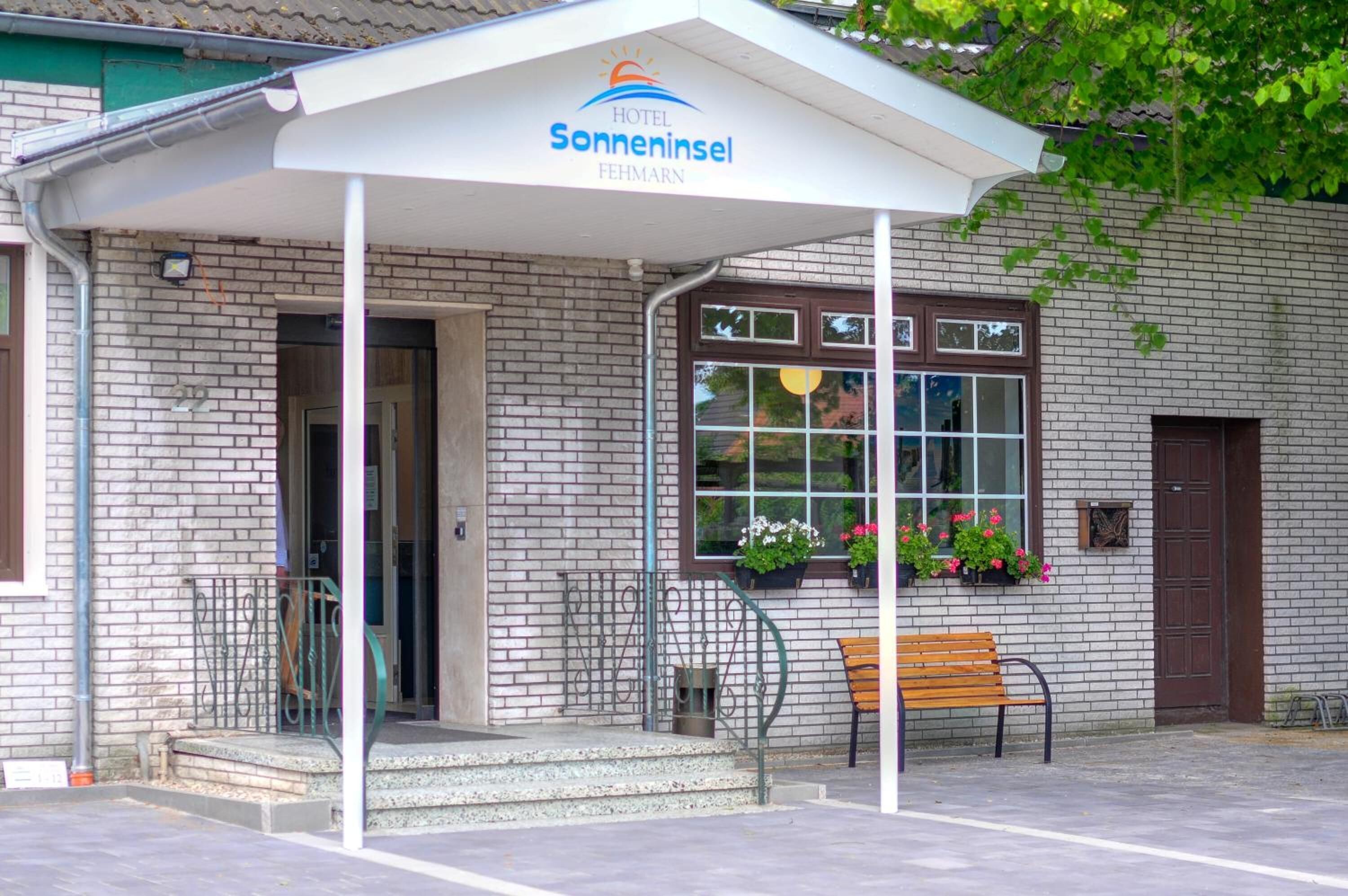 Een hotelingang met een overdekte veranda, een bankje en bloembakken.