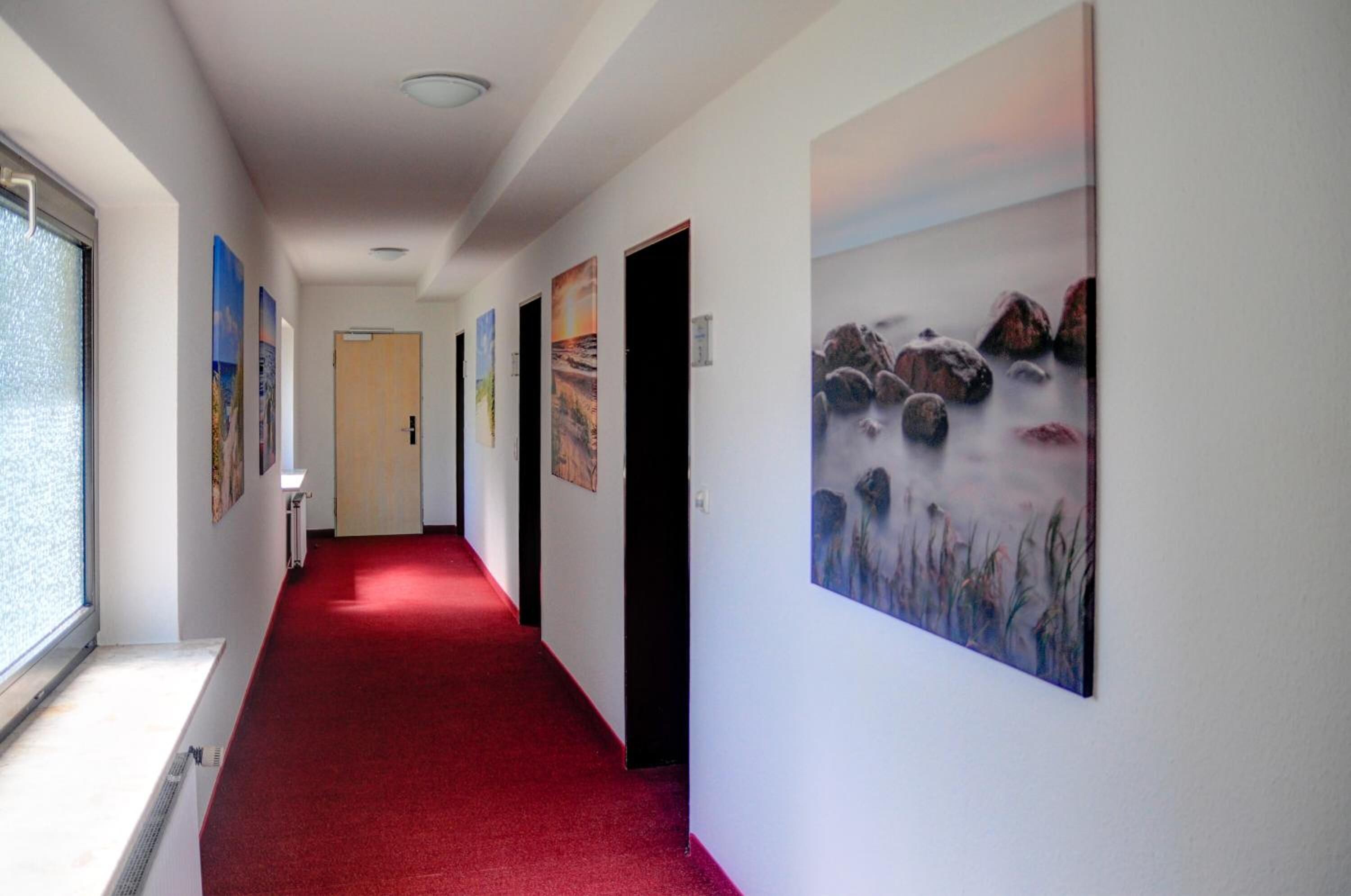 Ein Korridor mit rotem Teppich, weißen Wänden und verschiedenen gerahmten Kunstwerken.