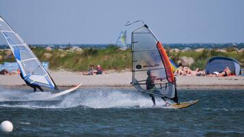 Zwei Windsurfer am Strand, im Hintergrund Zelte und Personen.