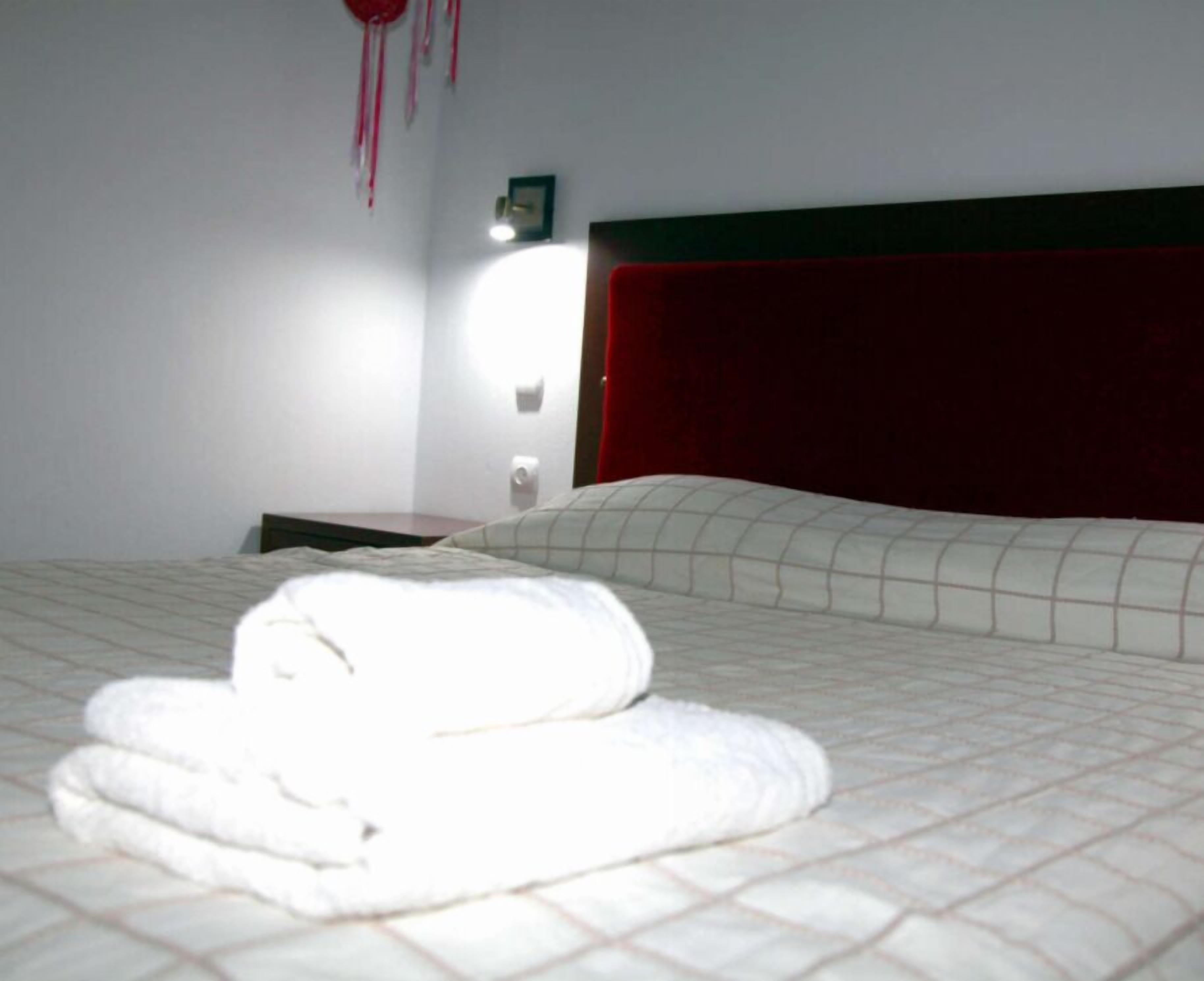 Una habitación de hotel con una cama bien hecha, cabecera roja y una lámpara fijada a la pared.