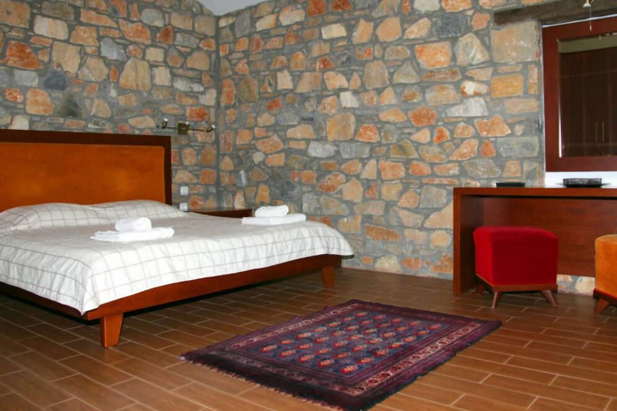 Een slaapkamer met een stenen muur, een bed met twee kussens, een rode stoel en een televisie op een houten bureau.
