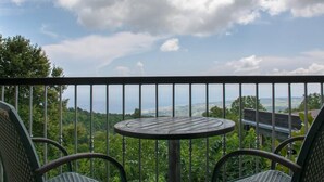 Een balkon met een ronde tafel en twee stoelen, met uitzicht op een weelderig landschap en verre horizon.