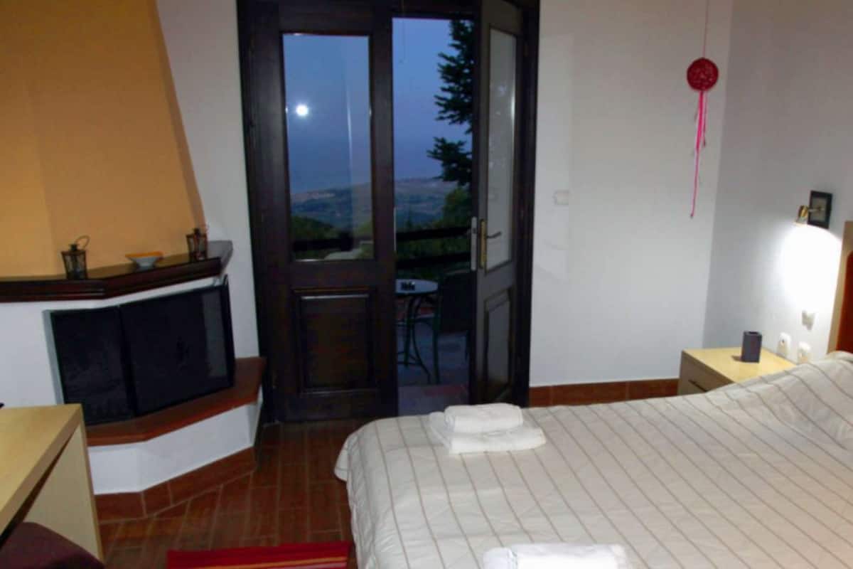 Een slaapkamer met een bed, een nachtkastje, een dressoir, een raam en een deur die leidt naar een balkon.