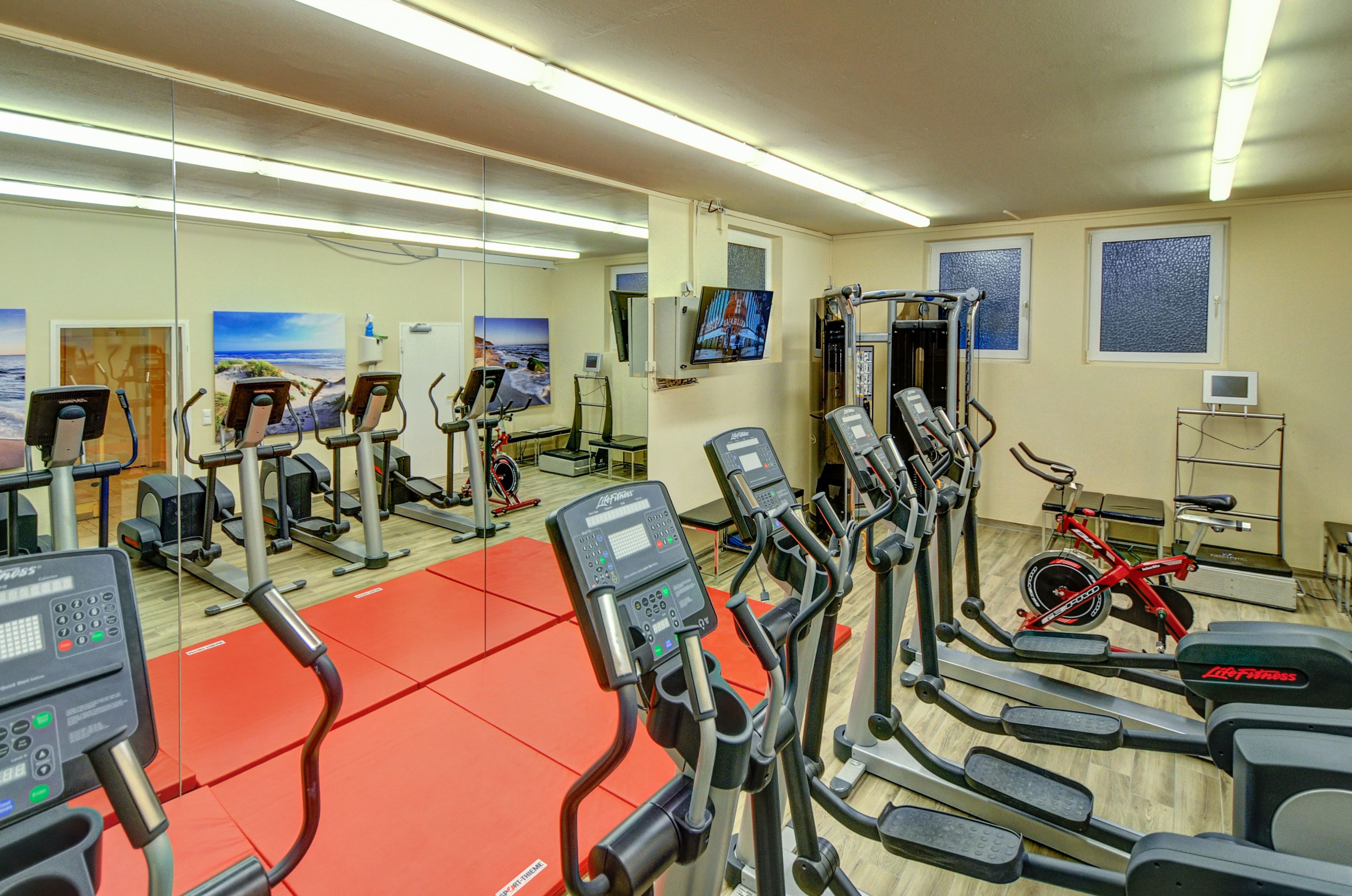 Une salle de sport équipée de divers appareils d’exercice, d’un espace avec des tapis rouges et d’un vélo.