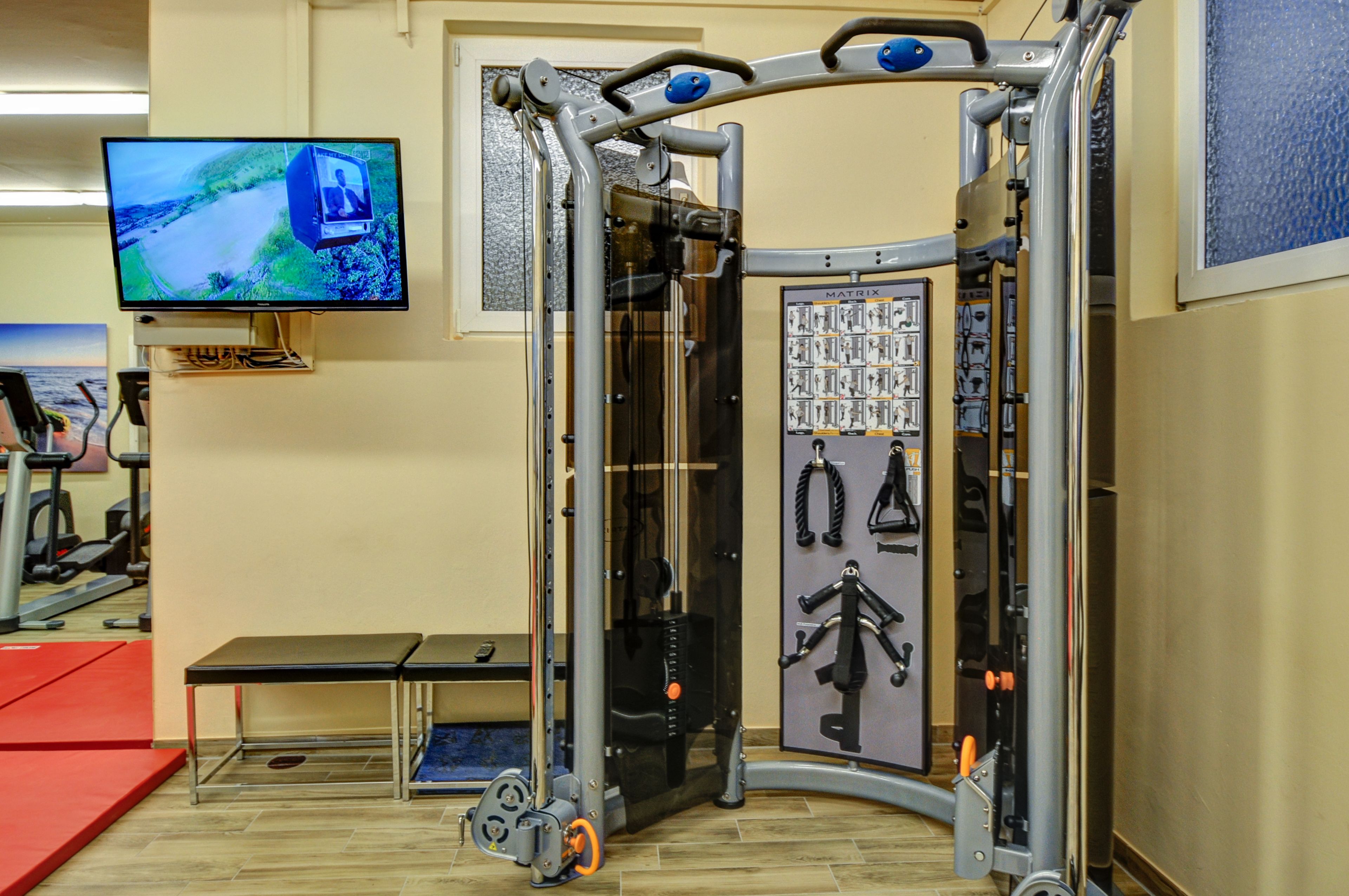 A gym with a pull-up bar, weight stack, and a television displaying a scenic view.