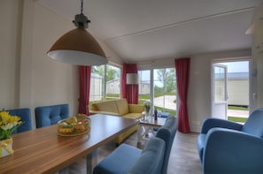 Ein modernes Wohnzimmer mit einem Holzespeisetisch, blauen Stühlen, einem gelben Sofa und einem großen Fenster mit roten Vorhängen.