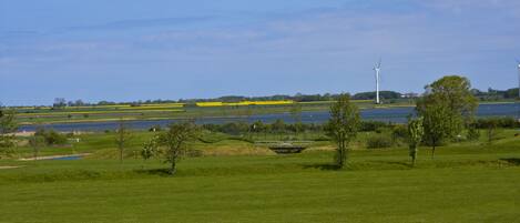 Un parcours de golf avec un plan d’eau et des éoliennes en arrière-plan.