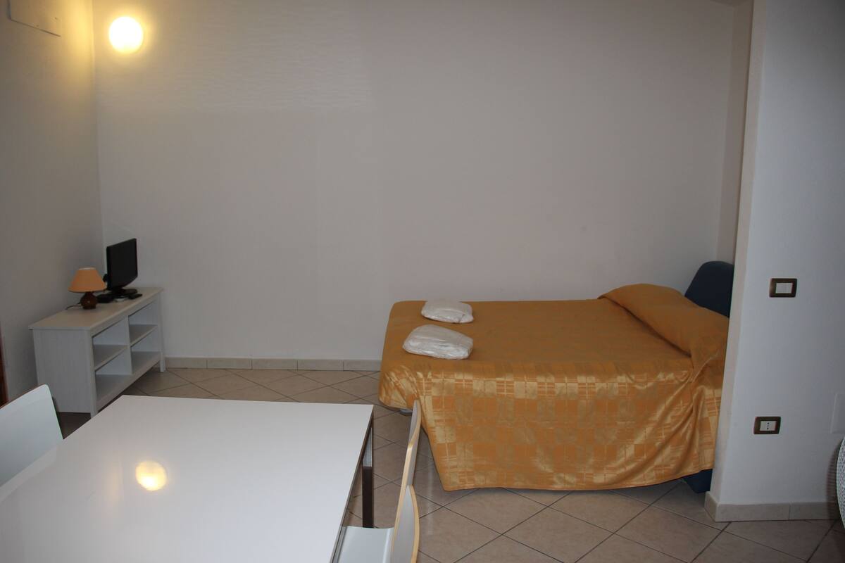 A small, clean room with a bed, a desk, and a chair.
