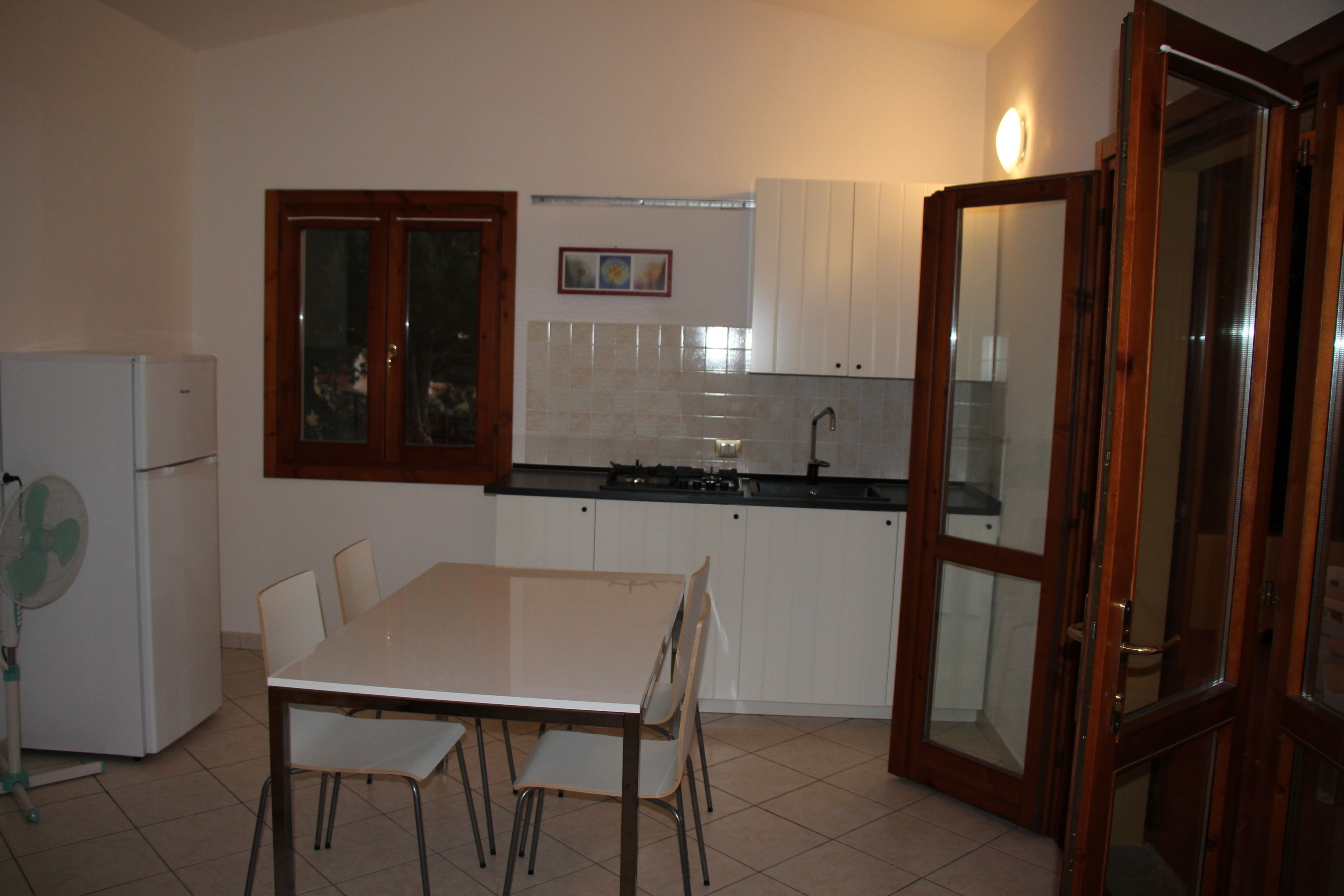 A compact kitchen with white cabinets, a dining table with chairs, and a refrigerator.