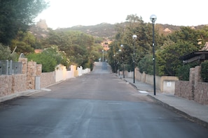 A street lined with stone walls and trees, leading to a hilly area with buildings. - Rena Majore Resort (Aglientu)