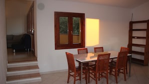 Un área de comedor con una mesa y sillas, un ventanal con vistas, y una escalera que lleva a otra habitación.