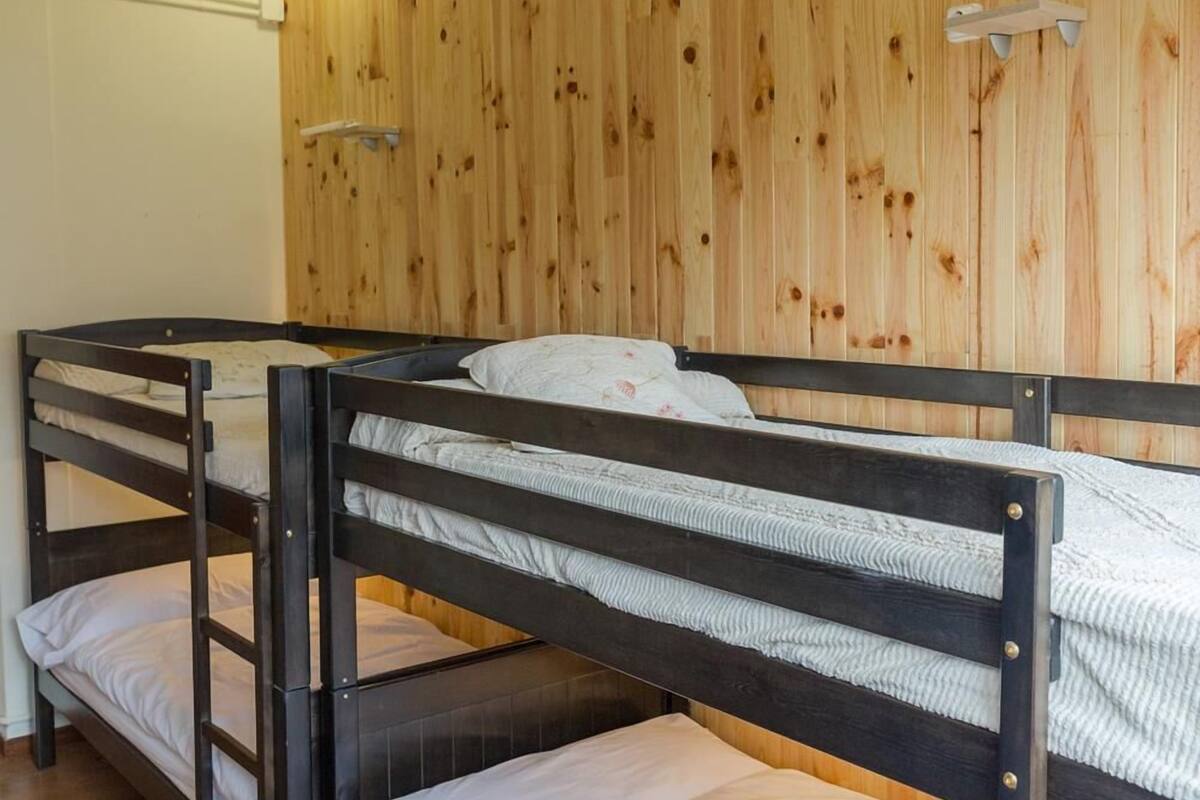 A room with three bunk beds, wooden walls, and two wall-mounted lights.