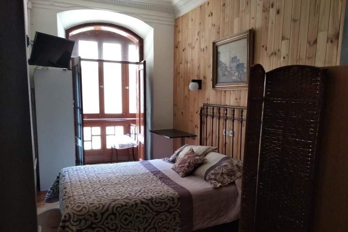 A bedroom with a bed, wooden paneling, a television, a framed picture, and a window with a view.