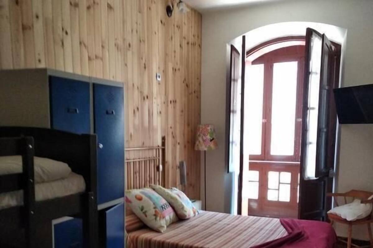 A room with a bunk bed, a desk, and a chair. There is a wooden wall and a window with a view.