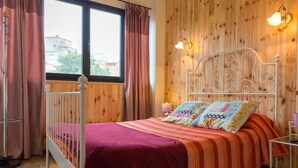 A bedroom with a wooden paneled wall, a white metal bed frame, a red bedspread, and two pillows with floral patterns. - Pensión La Fruta (Aviles)