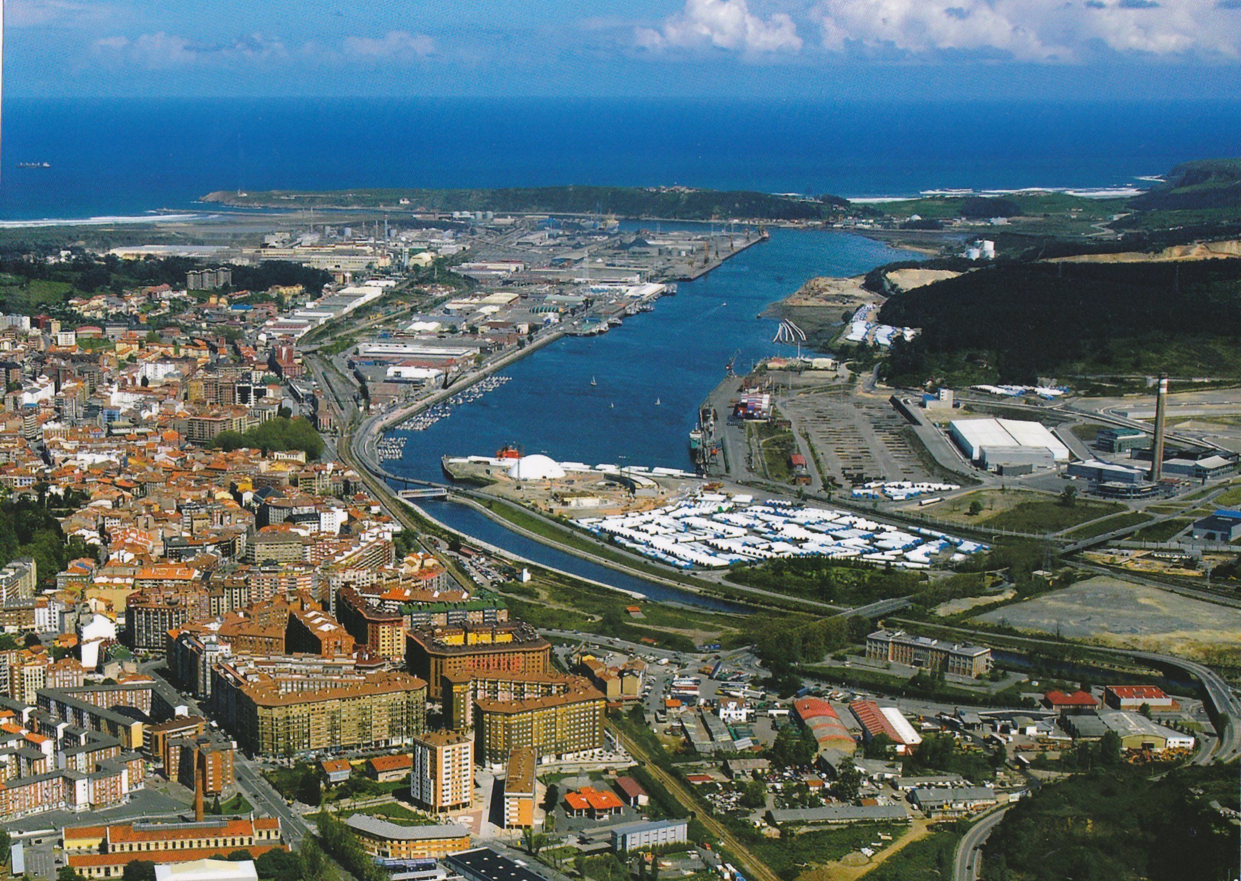 An aerial view of a coastal city with a marina, industrial area, and dense urban buildings. - Pensión La Fruta (Aviles)