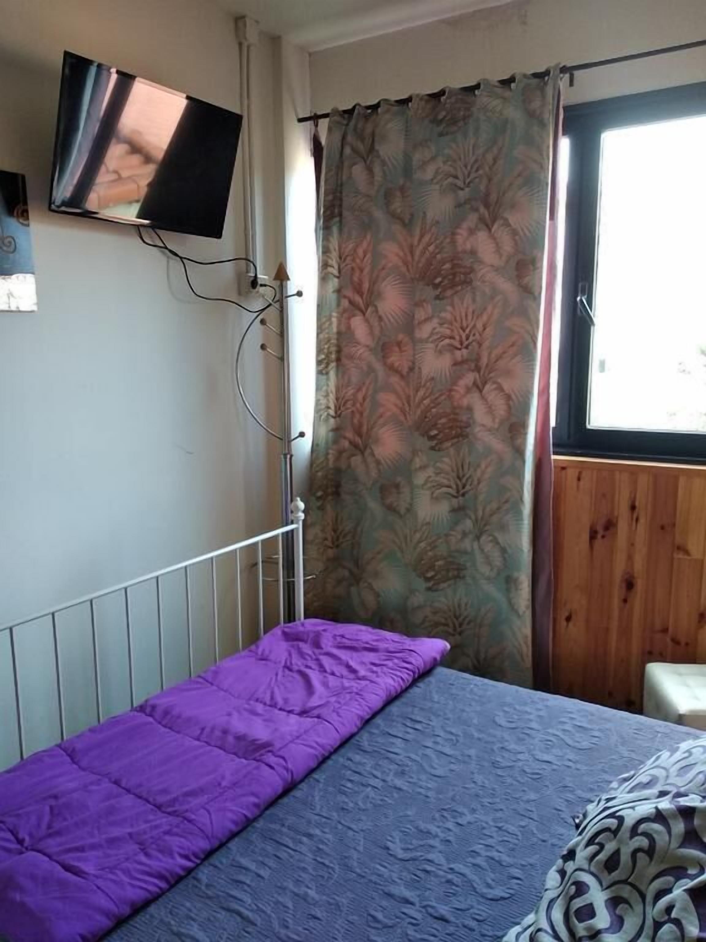 A room with a bed, a television mounted on the wall, and a window with curtains.