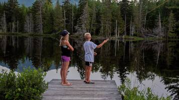 Two people standing on a wooden dock by a calm lake surrounded by dense forest.