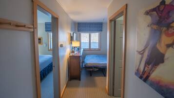 A narrow hallway leading to a bedroom with a bed, a dresser, and a window with blinds.
