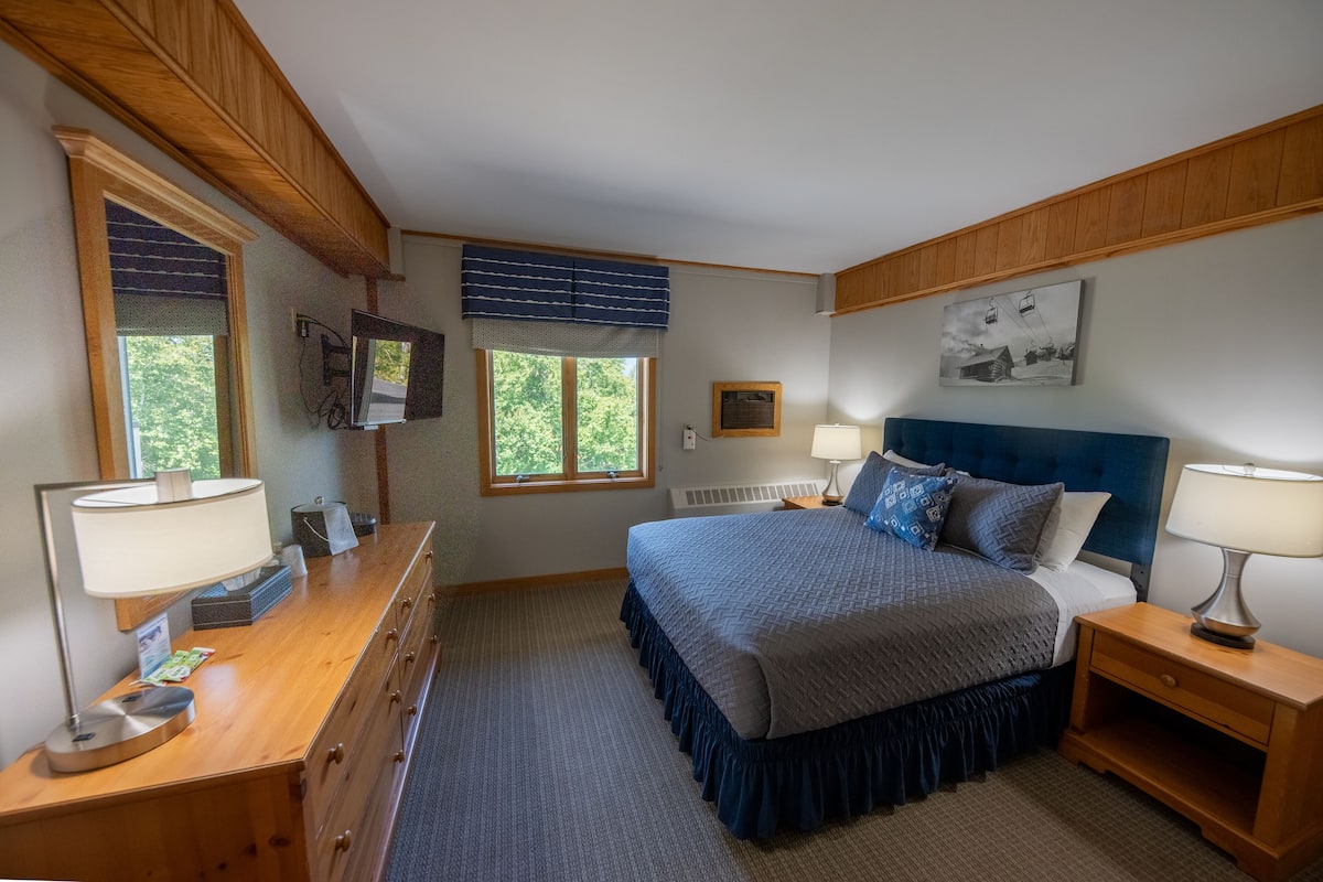 Un dormitorio con cama, cómoda, mesitas de noche y ventana.