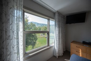 A room with a large window, a flat-screen TV mounted on the wall, and a wooden dresser.