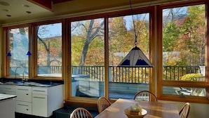 A modern kitchen with a large island, a dining area with a wooden table and chairs, and large windows with a view of trees and a balcony. - Sugarloaf Inn (Kingfield)