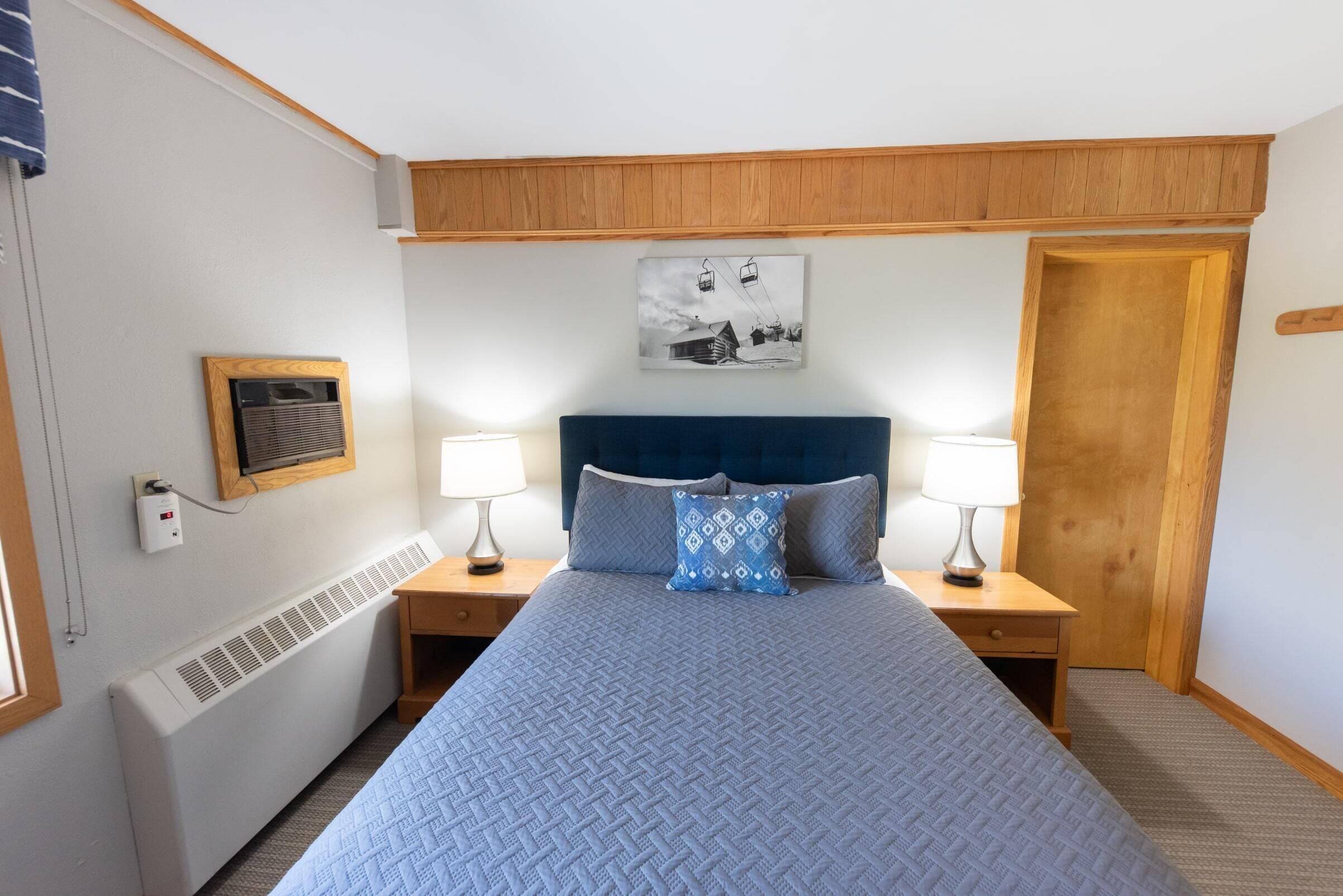 Een slaapkamer met een groot bed, twee nachtkastjes met lampen, een houten hoofdbord, een wandradiator, een ingelijst kunstwerk en een deur.