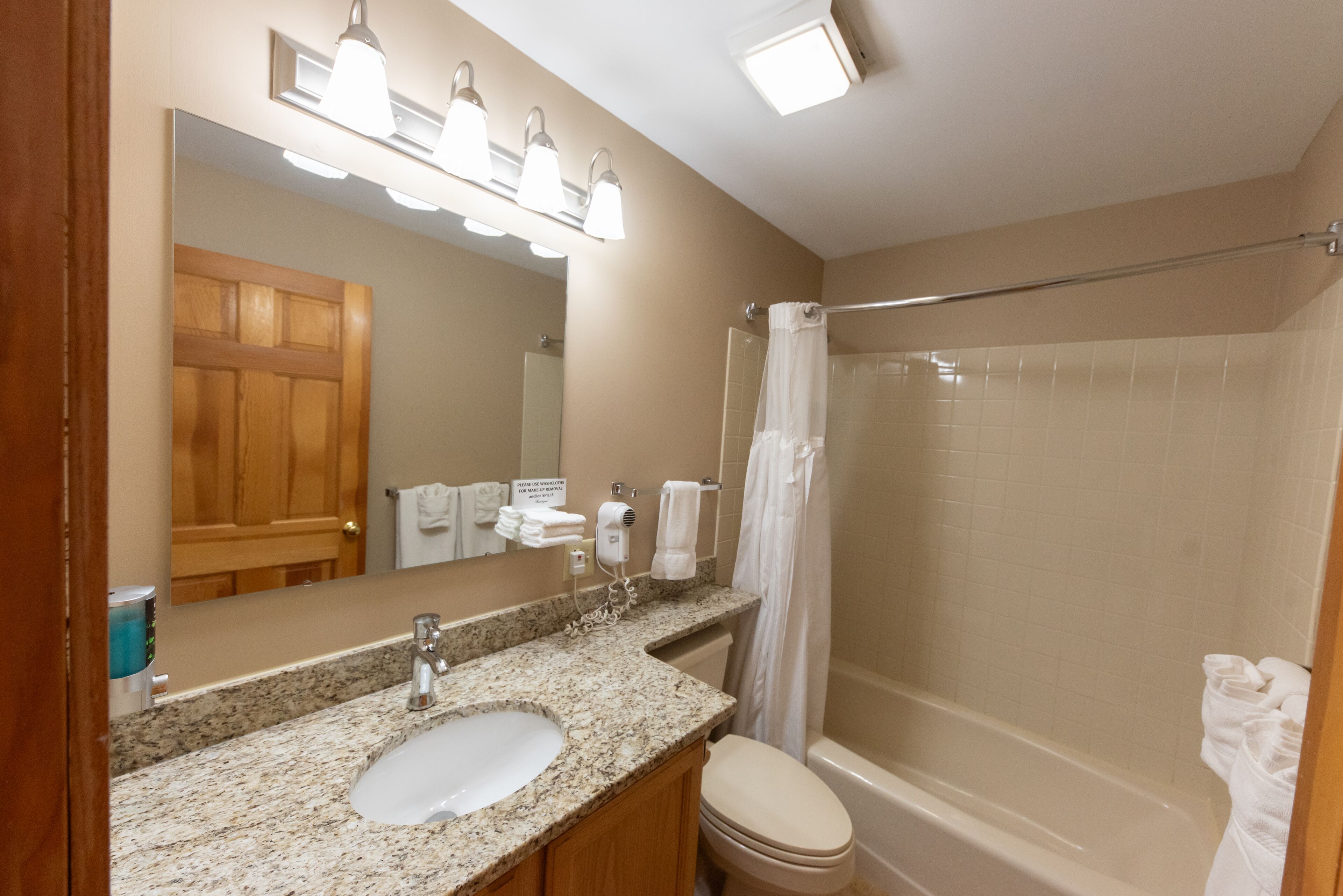 A bathroom with a granite countertop sink, a toilet, a bathtub, and a shower curtain.