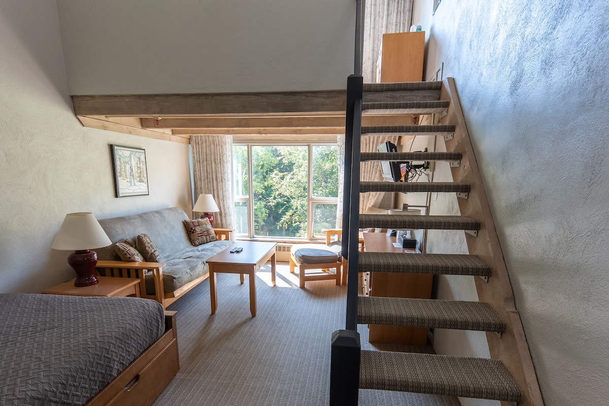 Una habitación acogedora con una cama, un sofá, una mesita y una escalera.