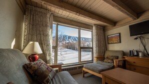 A cozy room with a large window, a sofa, a wooden table, and a television. - Sugarloaf Inn (Kingfield)