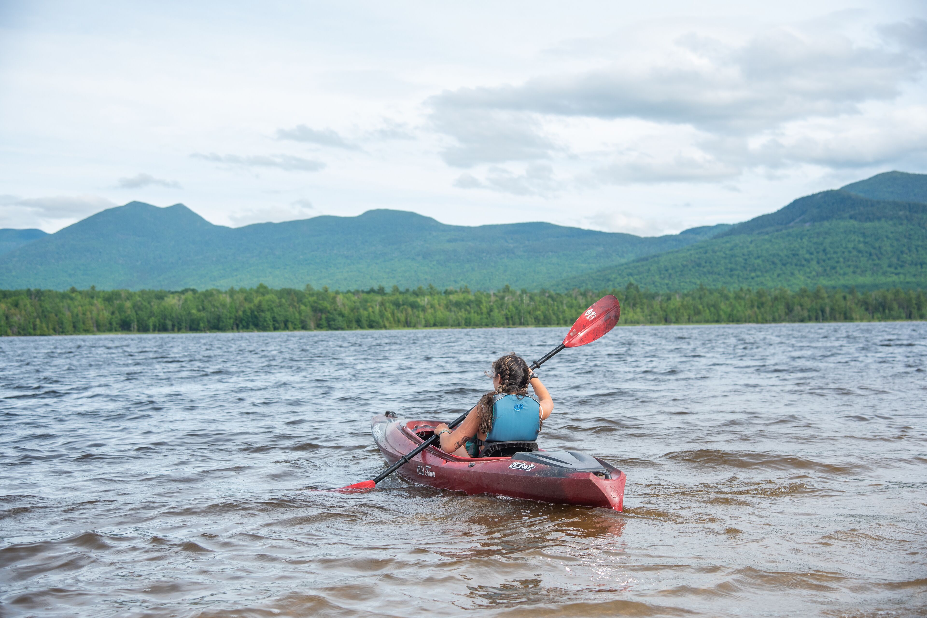 A person kayaking on a lake with mountains in the background.