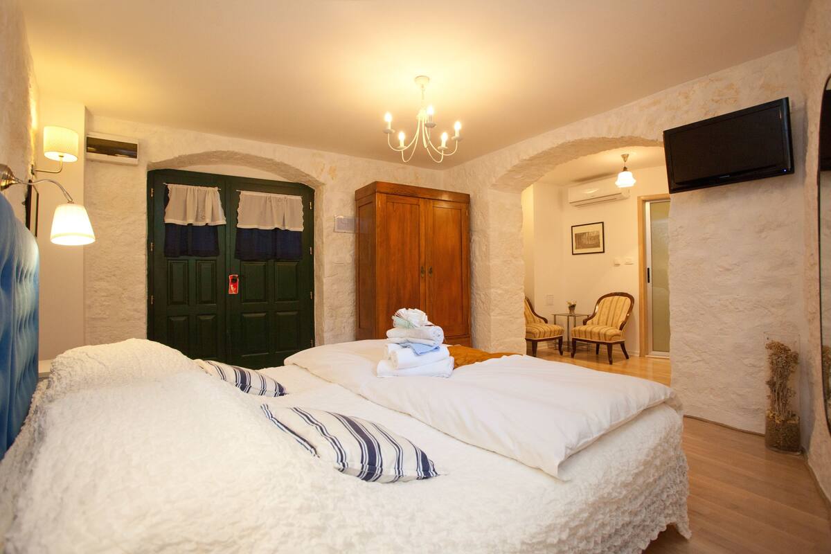 Un dormitorio con una cama grande, un armario de madera, un televisor montado en la pared y una mesita con una silla.