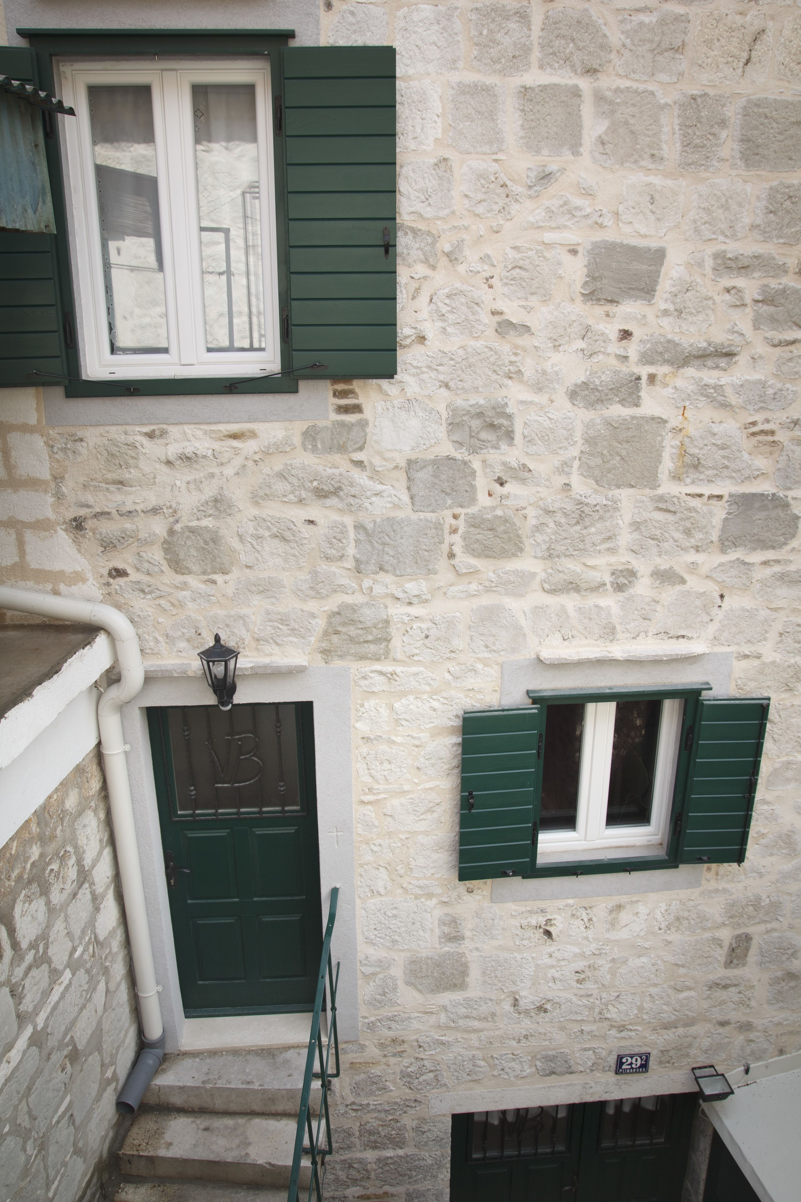 A stone building with a green door, a window with green shutters, and a small balcony.