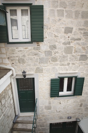 Un bâtiment en pierre avec une porte verte, une fenêtre avec des volets verts et un petit balcon.