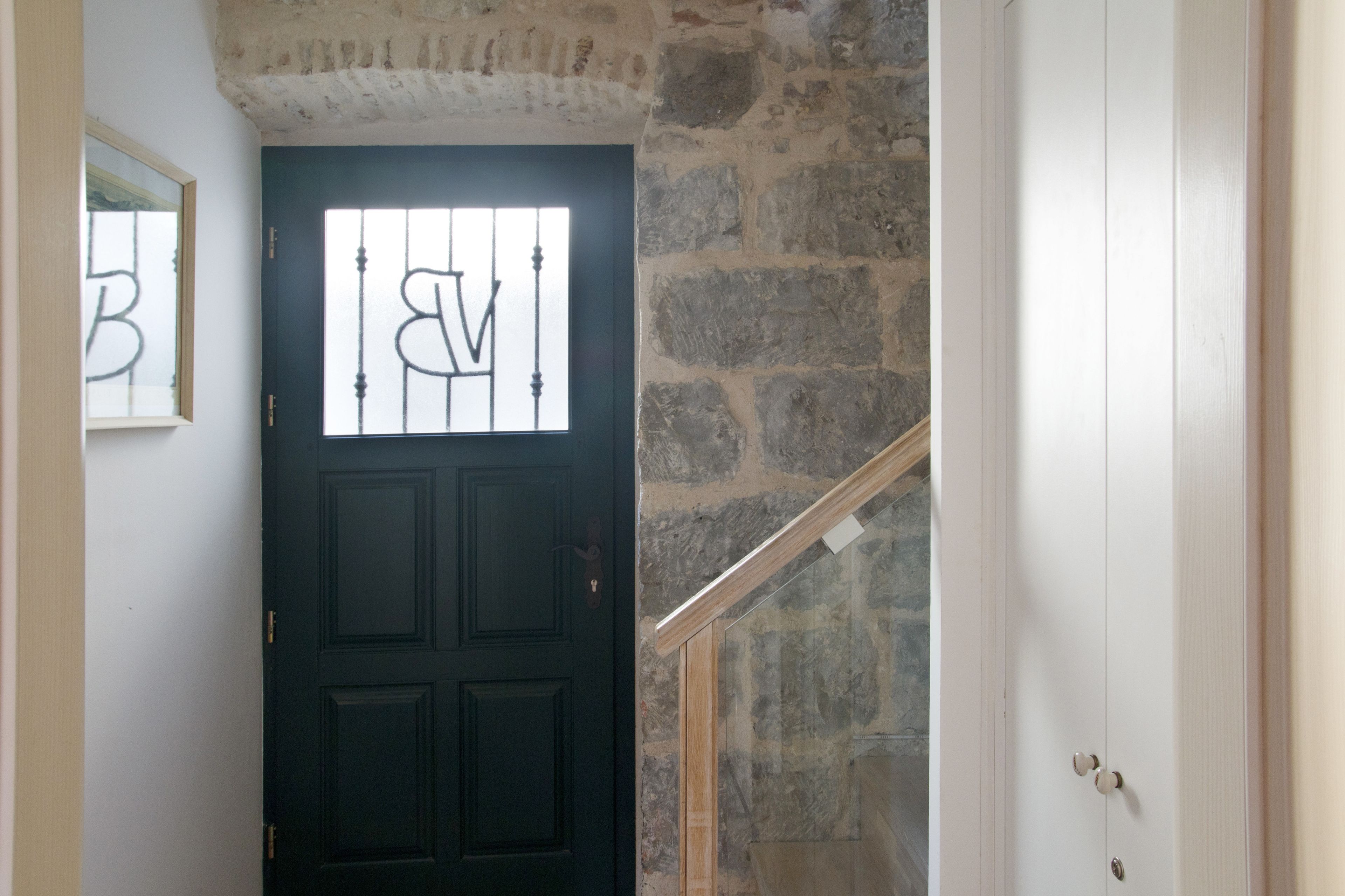 Una puerta negra con ventana, un muro de piedra y una escalera de madera.